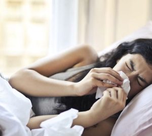 Bronchiectasia, quando tosse e catarro richiedono più attenzione: Una donna sdraiata a letto che starnutisce, illustrando i…