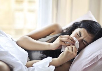 Bronchiectasia, quando tosse e catarro richiedono più attenzione: Una donna sdraiata a letto che starnutisce, illustrando i…