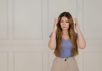 Quando un’otite si complica, possono comparire i segni della mastoidite: Giovane donna che segna con gli occhi chiusi…